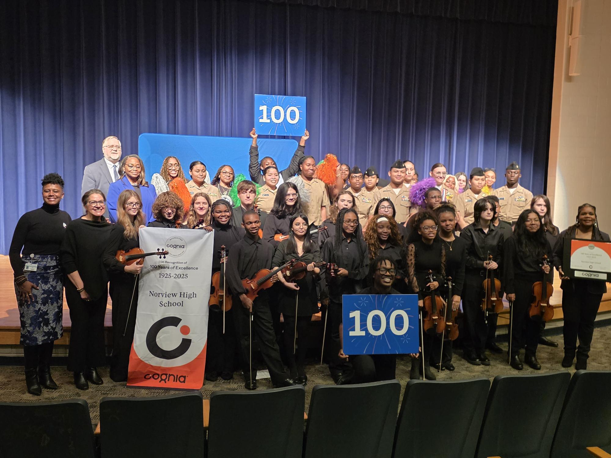 A group photo of the NHS JROTC (back), NHS Orchestra (front), Assistant Principal Rogers (left), and Principal Jacobs-Sumbry on the right holding a Cognia certificate.